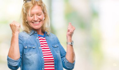 Gülümseyen ve başarı için çığlık orta yaş sarışın kadın izole arka plan çok mutlu ve heyecanlı kaldırdı, silah ile kazanan jest yapıyor. Kutlama kavramı.