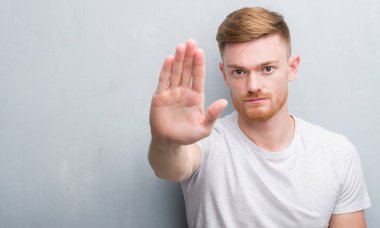 Genç Kızıl saçlı adam gri grunge duvar açık eliyle dur işareti ile ciddi ve kendine güvenen ifade, savunma hareketi yapıyor