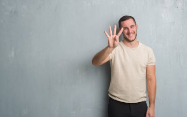 Beyaz delikanlı gösterilen ve parmakları ile işaret gri grunge duvarın üzerinden dört kendinden emin ve mutlu gülümseyerek iken numara.