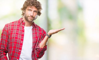 Yakışıklı İspanyol modeli adam neşeli sunulması ve kameraya bakarak avucunun ile işaret gülümseyen izole arka plan.