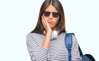 Kulaklıklar ve sırt çantası düşünme izole arka plan bakmaktan giyen genç Asyalı öğrenci kadın yorgun ve sıkılmış çapraz silah depresyon sorunları ile.