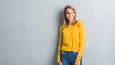 Grunge gri duvar uzak tarafına gülümseme ile yüzünde, doğal ifade seyir duran güzel genç kadın. Kendine güvenen gülüyor.