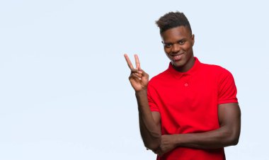 Afrikalı-Amerikalı genç mutlu yüz zafer işareti yaparken kameraya göz kırpıyor ile gülümseyen izole arka plan üzerinde. İki numaralı.