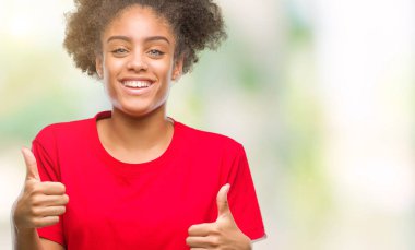 İzole arka plan başarı işareti el ile olumlu hareketi yaparken Genç afro Amerikan kadın başparmak gülümseyen ve mutlu. Neşeli bir ifadeyle, kazanan jest kameraya bakıyor.