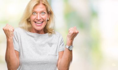 Orta yaş sarışın kadın kutluyor izole arka plan üzerinde şaşırttı ve başarı için kaldırdı kollarını açarak hayret ve gözleri açık. Kazanan kavramı.