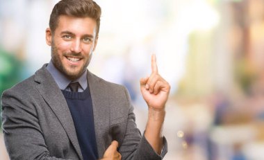 Kameraya bakarak yan el ve parmak ile işaret eden genç yakışıklı iş adamı yüzünde kocaman bir gülümseme ile izole arka plan üzerinde.