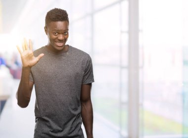 Gösterilen ve parmakları ile işaret gri t-shirt giyen genç Afro-Amerikan adam kendinden emin ve mutlu gülümseyerek süre beş numara.