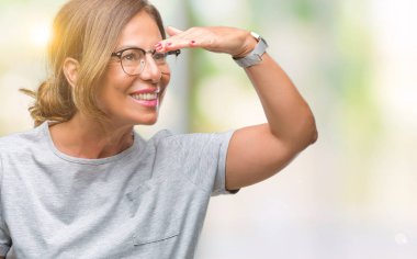 Üzerinde gözlük takan orta yaş İspanyol kadın kıdemli arka plan çok mutlu ve gülümseyen uzakta el ile üzerine kafa seyir izole. Arama kavramı.