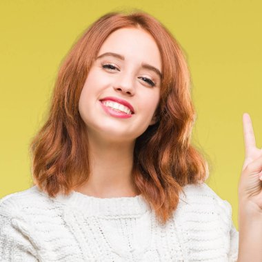 İzole arka plan mutlu yüz zafer işareti yaparken kameraya göz kırpıyor ile gülümseyen kış kazak giyen genç güzel kadın. İki numaralı.