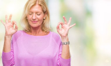 Orta yaş sarışın kadın izole arka plan üzerinde dinlenmek ve gülümseyen gözlerle parmak ile meditasyon jest yapıyor kapalı. Yoga kavramı.