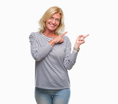 Orta yaş sarışın kadın gülümseyerek ve iki elleri ve parmakları ile tarafına işaret kamera bakarak izole arka plan üzerinde.