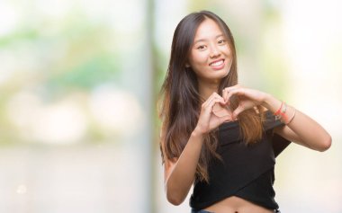 Genç Asyalı kadın kalp simgesi ve elleriyle şekil gösterilen aşık gülümseyen izole arka plan üzerinde. Romantik kavramı.