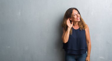 Bir işitme söylenti ya da dedikodu için dinleme kulak üzerinde el ile gülümseyen gri grunge duvarın üzerinden duran orta yaş İspanyol kadın. Sağırlık kavramı.