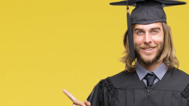Genç yakışıklı adam uzun saçlı yüzünde kocaman bir gülümseme ile izole arka plan üzerinde kameraya bakarak yan el ve parmak ile işaret mezun.