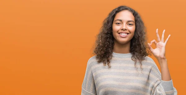 stock image Beautiful young hispanic woman wearing stripes sweater smiling positive doing ok sign with hand and fingers. Successful expression.