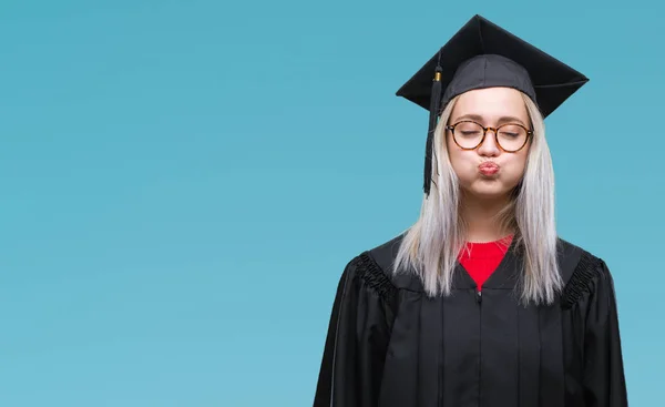 年轻的金发女子穿着毕业制服在孤立的背景下 膨化脸颊与滑稽的脸 嘴巴充气 疯狂的表情 — 图库照片