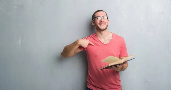 Young Caucasian Man Grey Grunge Wall Reading Book Surprise Face — Stock Photo, Image