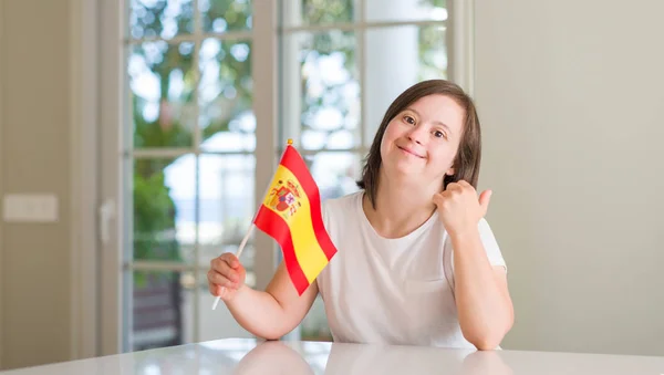 唐氏综合症妇女在家里拿着国旗的西班牙指着和显示与拇指与快乐的脸微笑的一面 — 图库照片