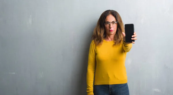 中年西班牙裔妇女显示 Smarphone 屏幕与自信的表情 聪明的脸认真思考 — 图库照片