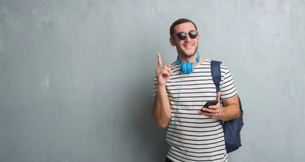 Junger Kaukasischer Student Über Graue Grunge Wand Mit Kopfhörer Smartphone — Stockfoto