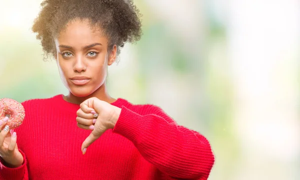 年轻的美国黑人妇女吃甜甜圈在孤立的背景与愤怒的面孔 消极标志显示不喜欢与拇指下来 拒绝概念 — 图库照片