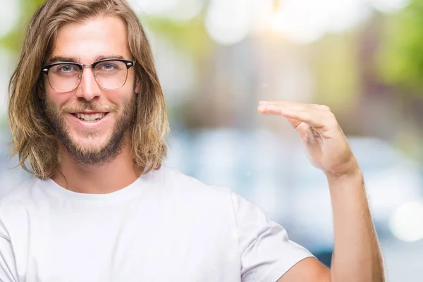 Young handsome man with long hair wearing glasses over isolated background gesturing with hands showing big and large size sign, measure symbol. Smiling looking at the camera. Measuring concept.