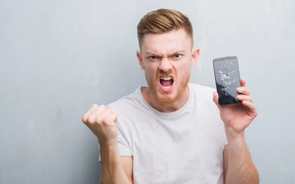 Joven Pelirrojo Sobre Gris Pared Grunge Sosteniendo Roto Teléfono Inteligente —  Fotos de Stock