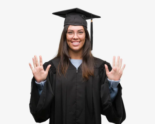 着た若いヒスパニック系女性卒業キャップと制服指で上向きの表示と番号を自信を持って 幸せな笑みを浮かべている間 — ストック写真