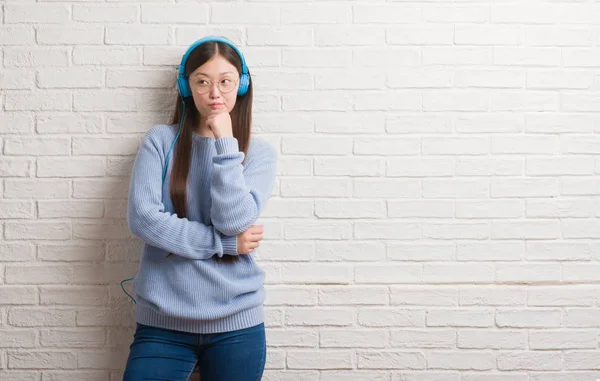 Unga Kinesiska Kvinnan Över Tegelvägg Bär Hörlurar Allvarligt Ansikte Funderar — Stockfoto