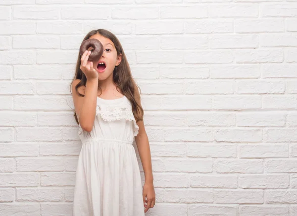 ヒスパニック系の子供白レンガ壁を食べる以上チョコレート ドーナツ驚き顔 恐怖表現と興奮とショックで怖い — ストック写真