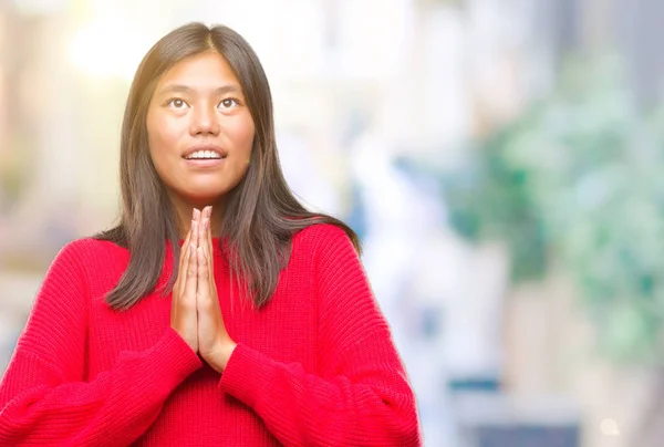 Young asian woman wearing winter sweater over isolated background begging and praying with hands together with hope expression on face very emotional and worried. Asking for forgiveness. Religion concept.