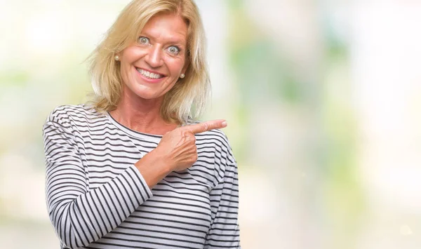 Middle age blonde woman over isolated background cheerful with a smile of face pointing with hand and finger up to the side with happy and natural expression on face looking at the camera.