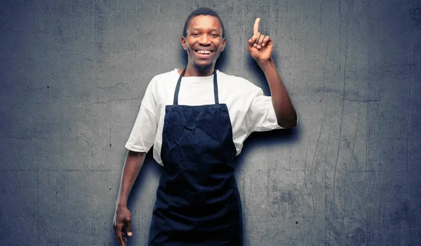 African man shop owner wearing apron pointing away side with finger