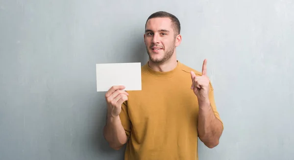 Joven Caucásico Hombre Sobre Gris Grunge Pared Celebración Tarjeta Blanco —  Fotos de Stock