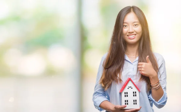 Young asian woman real state agent holding house isolated background happy with big smile doing ok sign, thumb up with fingers, excellent sign