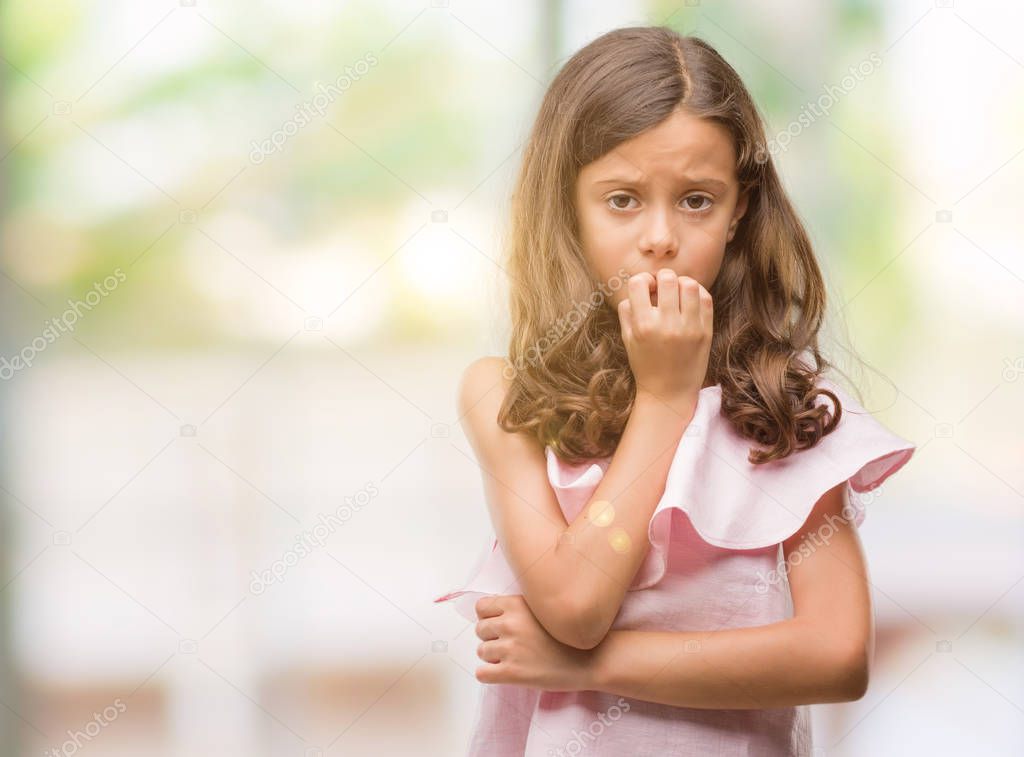 Brunette hispanic girl wearing pink dress looking stressed and nervous with hands on mouth biting nails. Anxiety problem.
