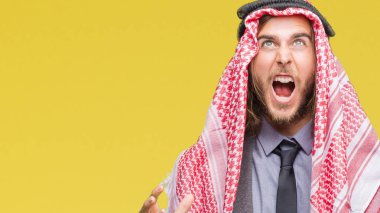 Genç yakışıklı Arap adam uzun saçlı izole arka plan çılgın ve kızgın bağırarak ve agresif ifade ve silah kaldırdı bağırmaya keffiyeh giyiyor. Hayal kırıklığı kavramı.