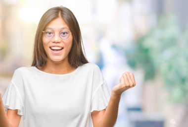 İzole arka plan üzerinde kutluyor gözlük takan Genç Asyalı kadın şaşırttı ve silah ile başarı için yükseltilmiş ve açık gözler hayrete düşürdü. Kazanan kavramı.