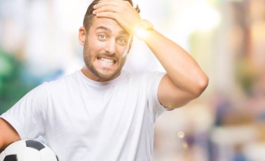 Baş, el ile vurguladı izole arka plan üzerinde futbol futbol topu tutan genç yakışıklı adam şok utanç ve sürpriz suratla, öfkeli ve sinirli. Korku ve hata için üzgün.