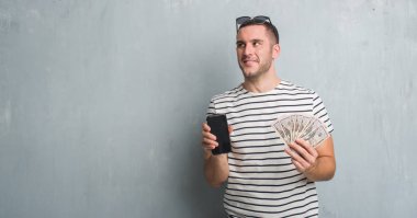 Dolar ve smarphone görünümlü yan ve dik dik bakma uzağa düşünce gülümseyen tutan gri grunge duvarın üzerinden beyaz delikanlı.