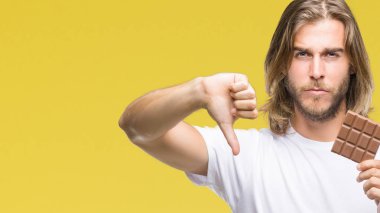 Uzun saç beslenme ile genç yakışıklı adam kızgın yüzü, eksi işareti aşağı antipati başparmak ile gösterilen, ret kavramı ile izole arka plan üzerinde çikolata bar