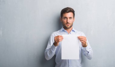 Boş kağıt sayfası sözleşme kendine güvenen bir ifade ile acımak yüz ciddi düşünüyorum tutarak gri grunge duvarın üzerinden yakışıklı genç