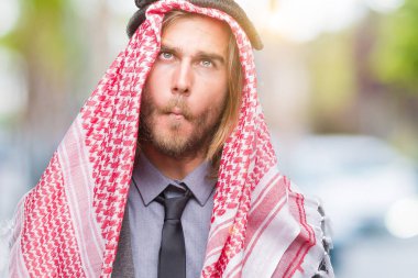 Genç yakışıklı Arap adam uzun saçlı izole arka plan yapma balık yüzüne dudaklı, çılgın ve komik bir jest keffiyeh giyiyor. Komik ifade.