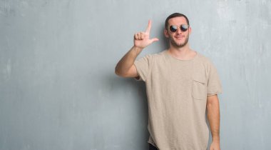 Beyaz delikanlı gösterilen ve parmakları ile işaret güneş gözlüğü takıyor gri grunge duvarın üzerinden ikincisi ise kendinden emin ve mutlu gülümseyerek.