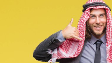 Uzun saçlı keffiyeh yapıyor gülümseyen izole arka plan üzerinde giyen genç Arap yakışıklı telefon hareketi ile el ve parmak telefonda konuşuyor gibi. Kavramları iletişim.