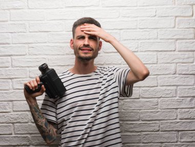 Genç adam filme kafasına, utanç ile şok el ve yüz, öfkeli ve sinirli sürpriz ile vurguladı beyaz tuğla duvarın üzerinden video kamera ayakta tutan. Korku ve hata için üzgün.