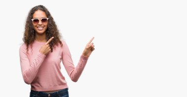 Güzel genç İspanyol kadın gülümseyerek ve iki elleri ve parmakları ile tarafına işaret kamera bakarak güneş gözlüğü takıyor.