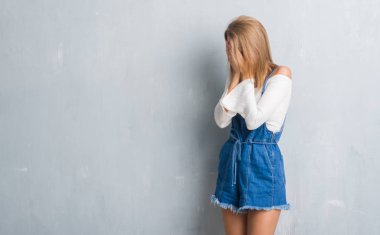 Yüzünü elleriyle ağlayarak süre kapsayan üzgün ifade ile grunge gri duvardan duran güzel genç kadın. Depresyon kavramı.