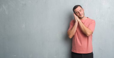 Uyku yorgun hayal ve eller ile birlikte kapalı gözlerle gülümseyerek poz gri grunge duvarın üzerinden beyaz delikanlı.