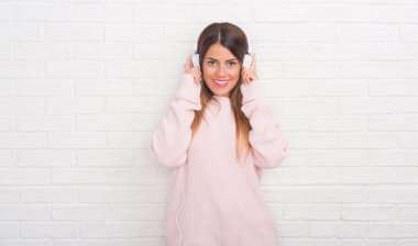 Beyaz tuğla duvar müzik ve ayakta ve diş gösterilen kendine güvenen bir gülümsemeyle gülümseyerek mutlu bir yüz ile dans kulaklıklar giyen genç yetişkin kadın